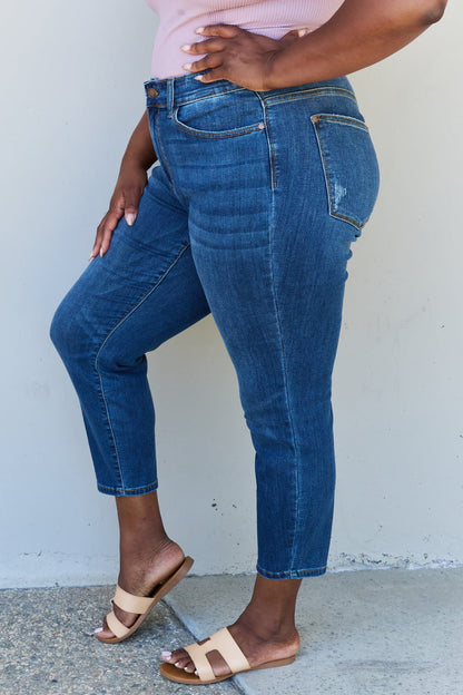 A woman wearing Judy Blue Aila Regular Mid Rise Cropped Relax Fit Jeans, exuding casual chic style. The jeans offer a relaxed fit and feature a flattering mid-rise waist, providing comfortable everyday wear. Their cropped length adds a modern touch, allowing for a showcase of your favorite footwear.