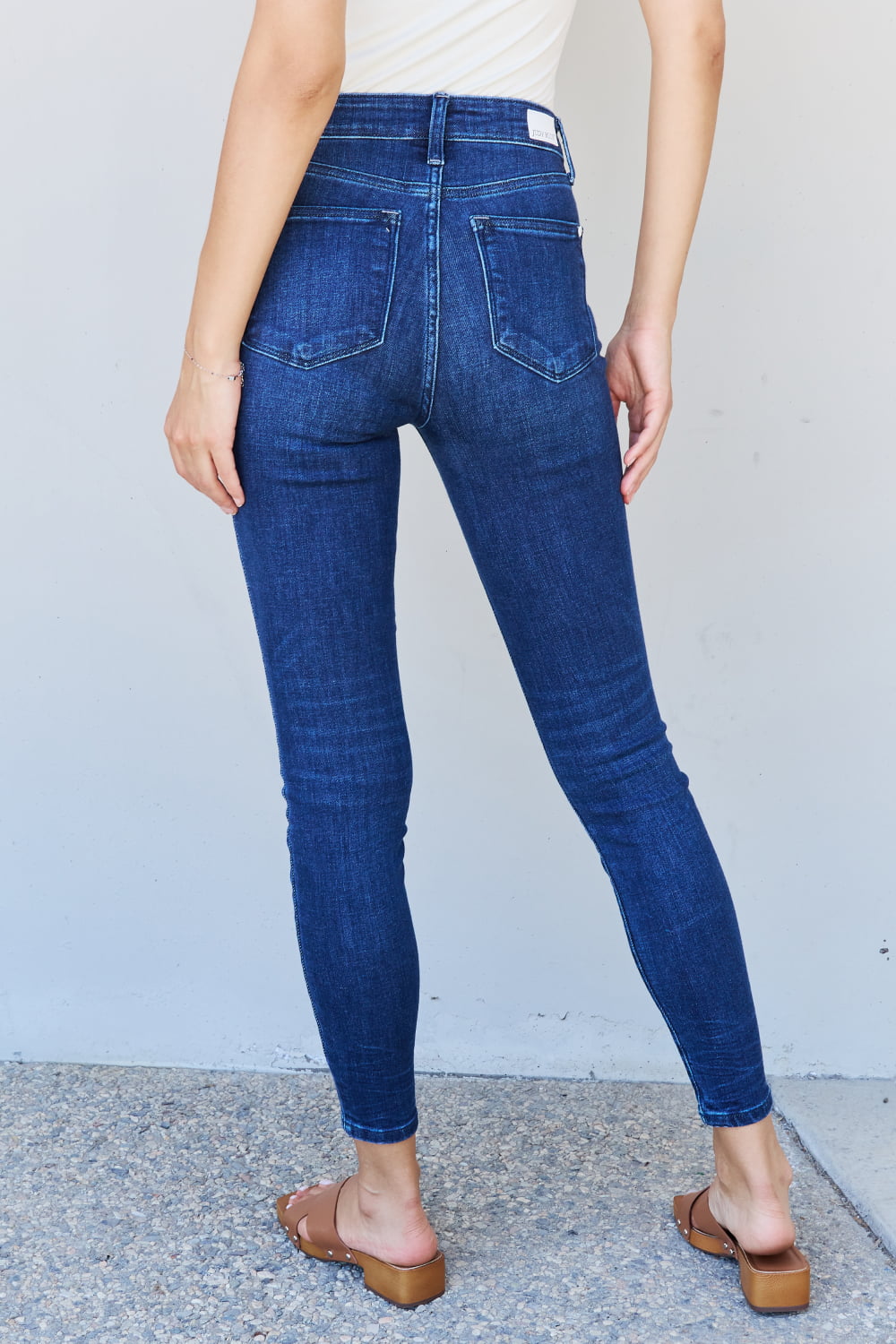 A woman stepping into effortless edge with Judy Blue Marie Full Size Mid Rise Crinkle Ankle Detail Skinny Jeans. The jeans showcase a mid-rise design and crinkle ankle detailing, adding a unique and stylish touch. Made with quality denim, they promise both comfort and durability. 