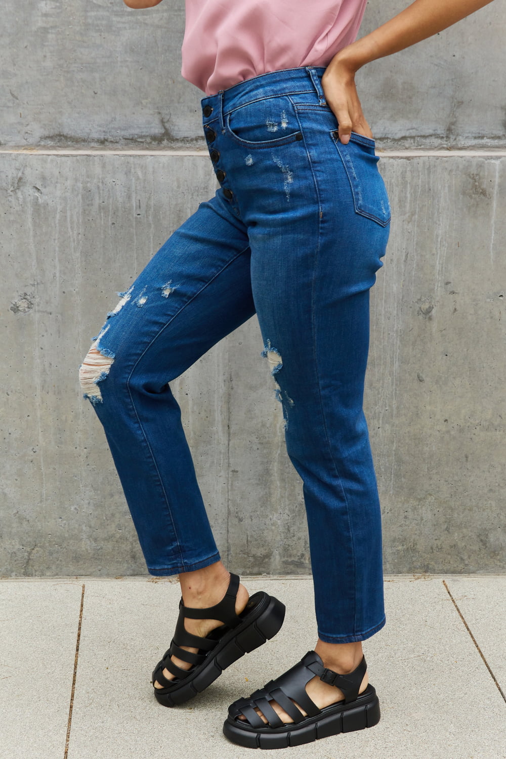 A woman experiencing chic and edgy style with Judy Blue Melanie Full Size High Waisted Distressed Boyfriend Jeans. The jeans showcase a high-waisted design and a trendy distressed look, making a fashionable statement. Made with quality denim, they guarantee both comfort and durability. The relaxed fit adds a touch of casual charm, ideal for everyday wear. 